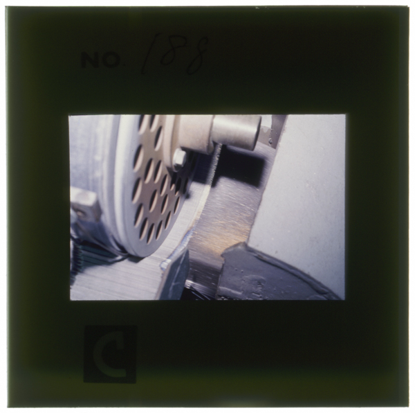 先頭研磨。鋼線をロールで送りながら回転砥石に接触させ、先を研磨する。